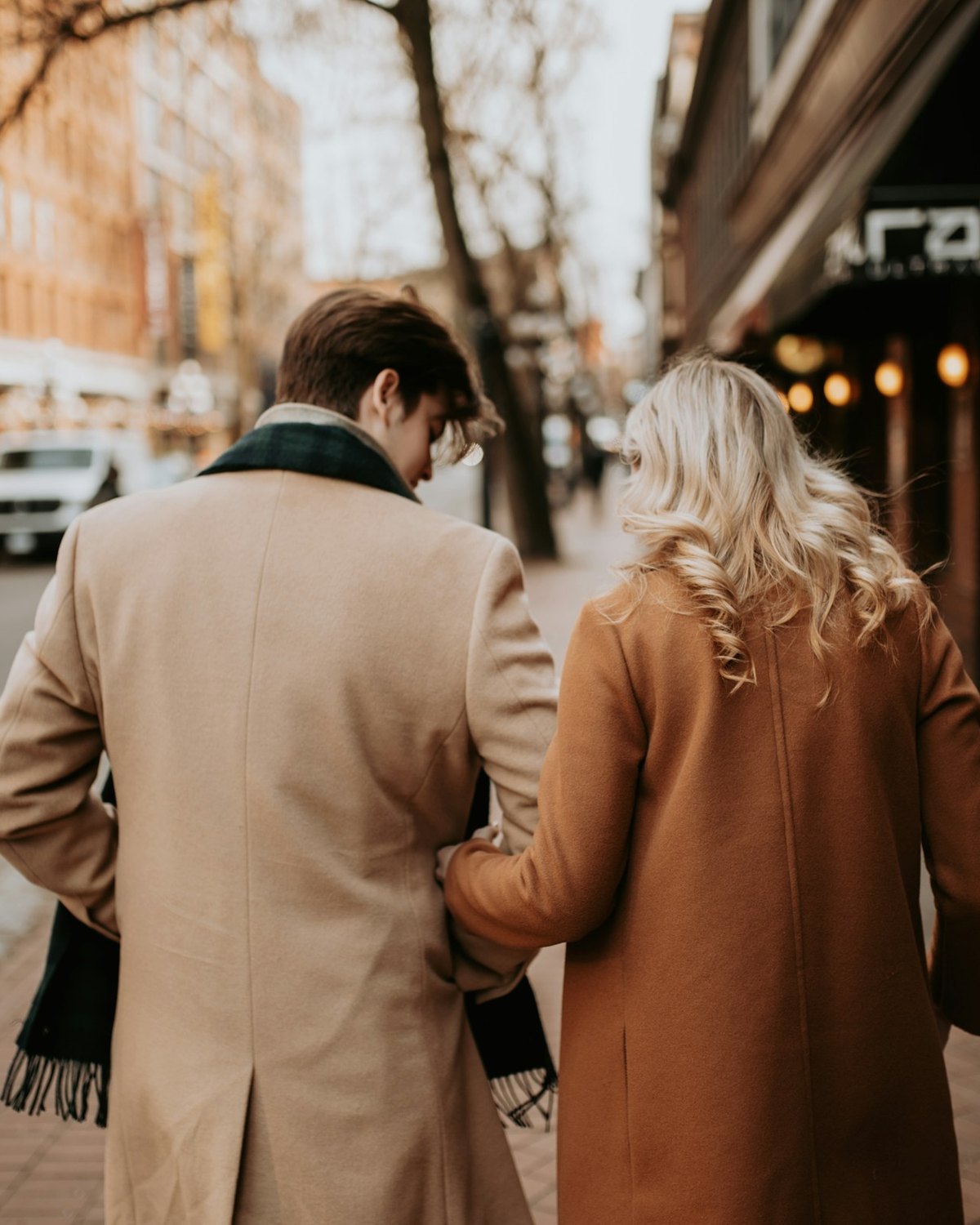 A couple in camel coats walking arm in arm down a city street